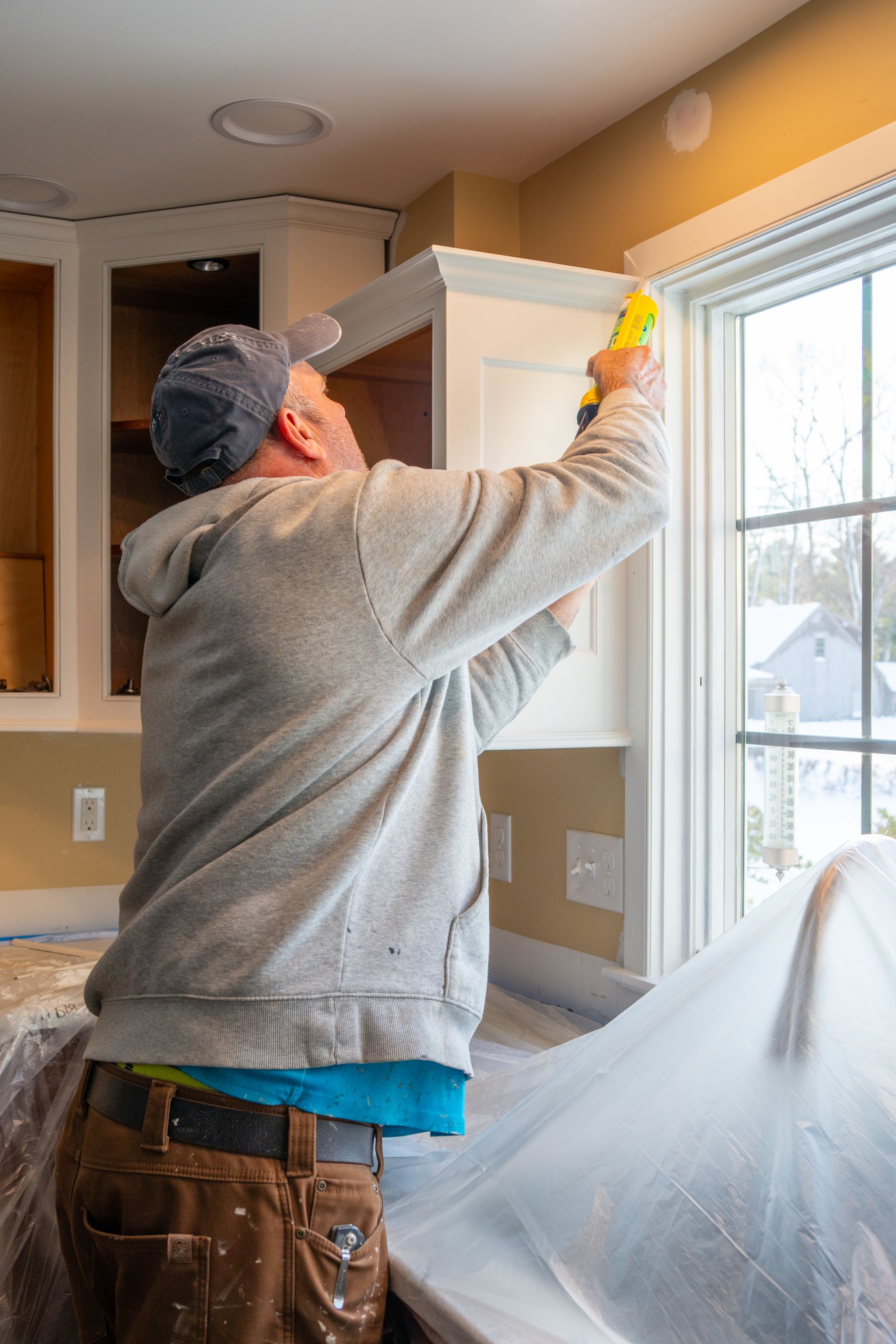 Contractor caulking trim around newly installed kitchen cabinetry